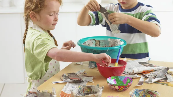 Two children making papier-mâché at a kitchen table